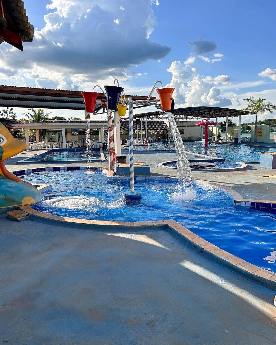 Water playground with colorful buckets pouring water into a swimming pool under a cloudy blue sky.